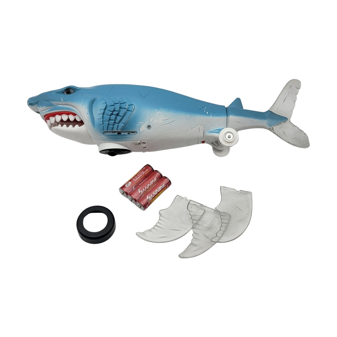 Bump n go shark featuring an open mouth with visible inner components, three detachable fins, powered by two AA batteries, and a black ring on a white background.