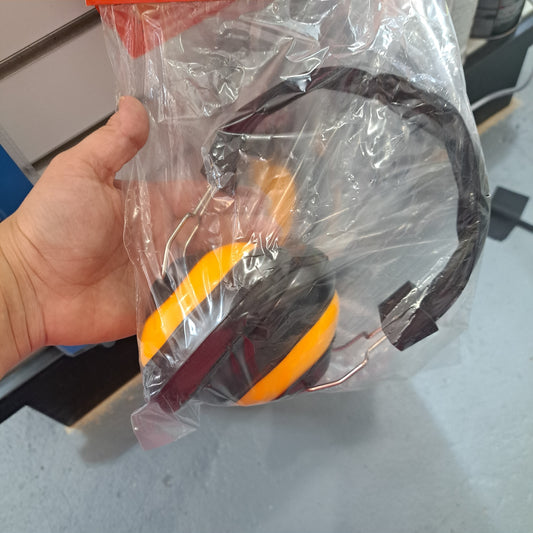 A hand holding a pair of ear protection muffs, designed in orange and black, inside a clear plastic bag.