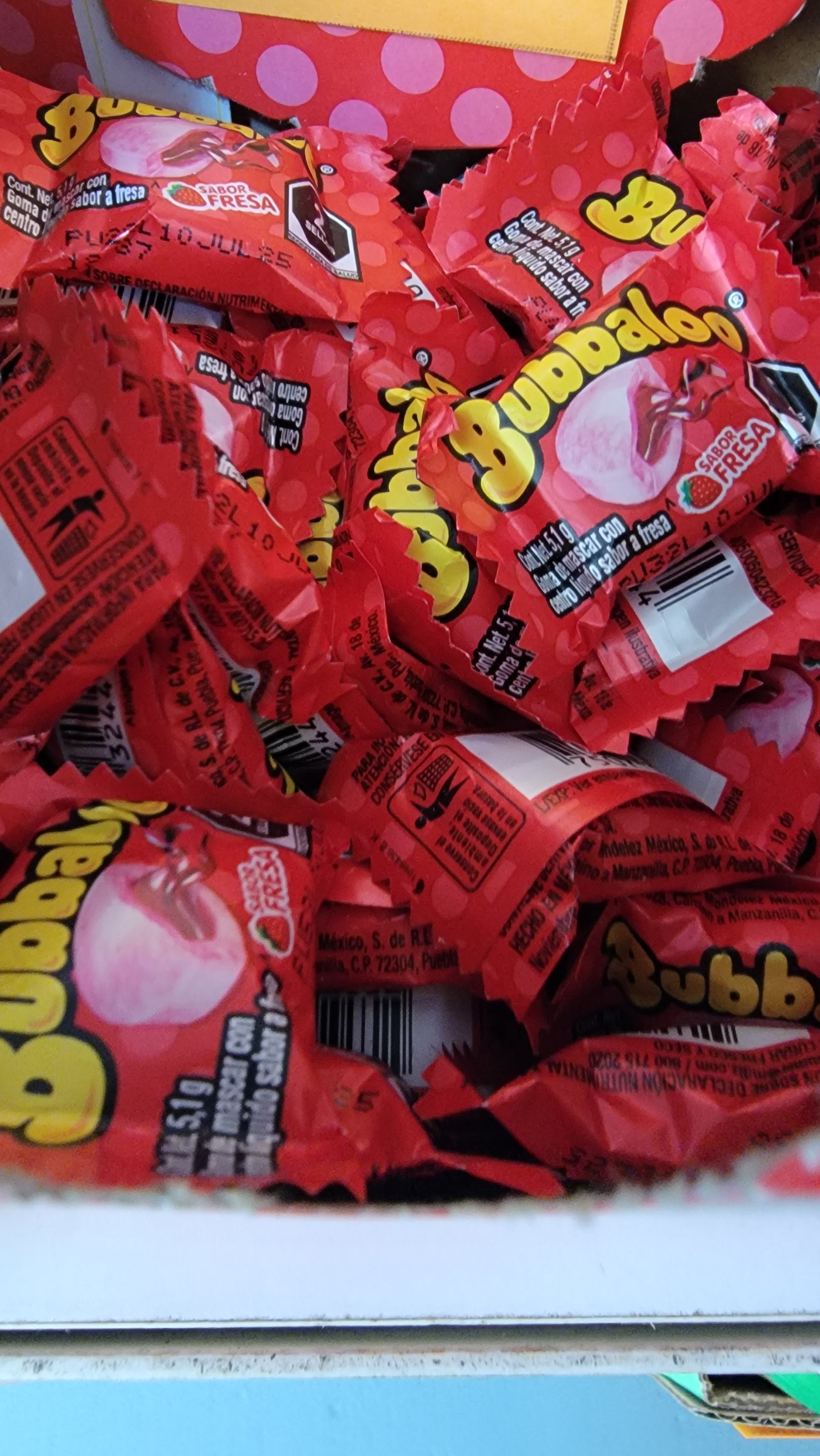 A heap of Bubbaloo Strawberry bubble gum, each individually wrapped in red packaging with a strawberry flavor graphic and text.