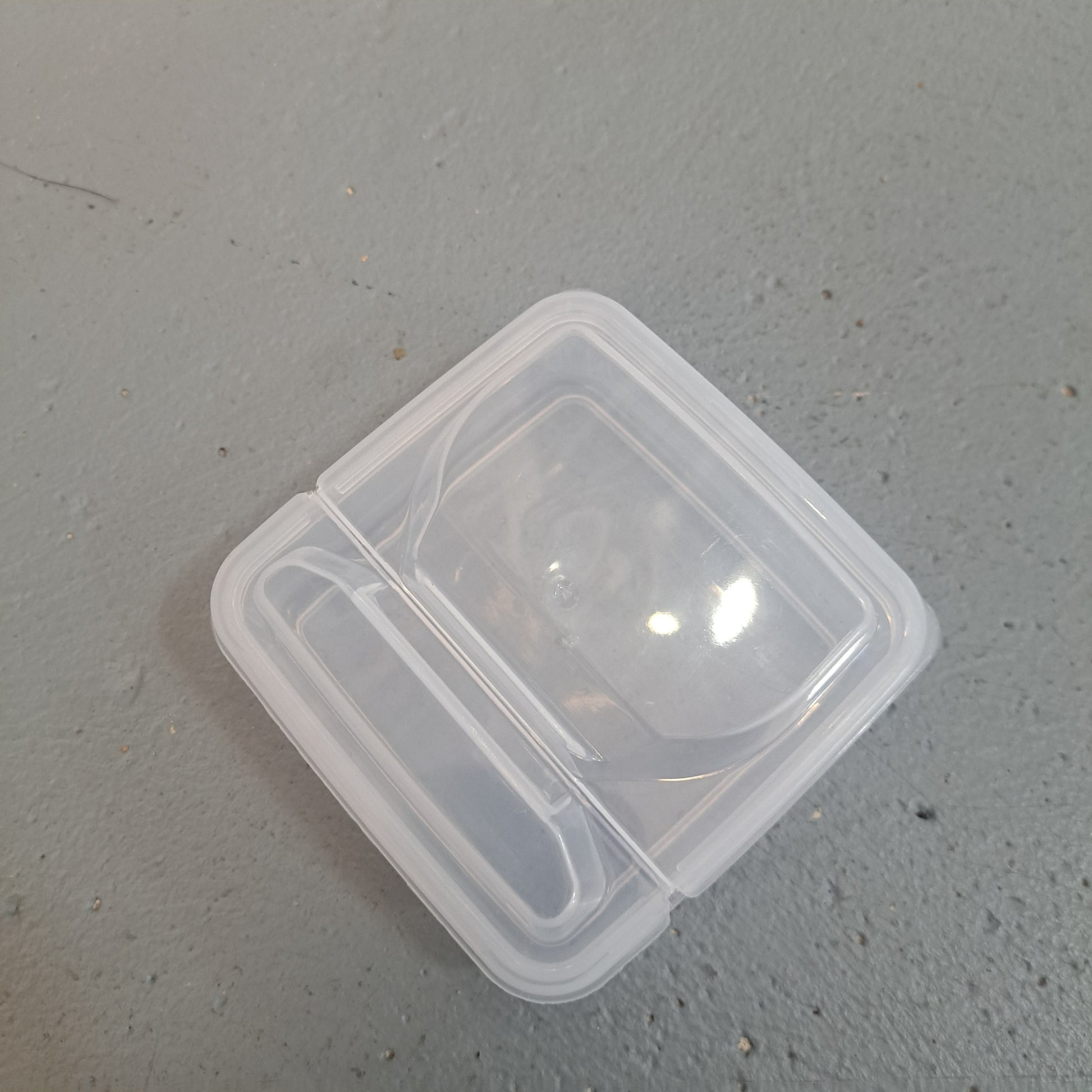 A sandwich container, small and transparent with a tightly sealed lid, is placed on a gray surface.