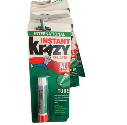 A hand holding a blister pack of Instant All Purpose Tubes of Krazy Glue with a tube inside, displayed on a store rack. The packaging highlights its one-drop applicator and various uses.