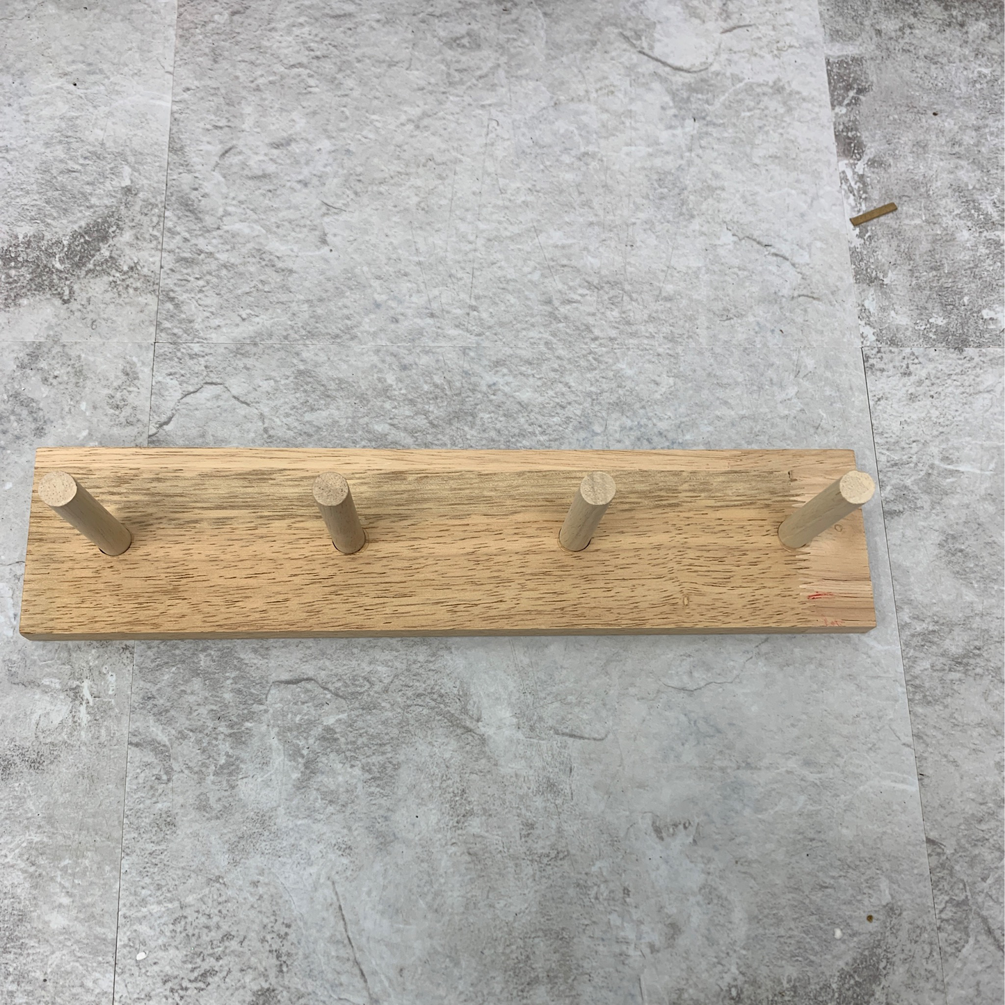 A Natural wood peg holder featuring four cylindrical pegs mounted on a square, weathered concrete base.