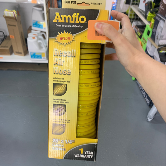 A person holds a boxed recoil air hose 1/4" 25' made of nylon, with specifications and a 1-year warranty displayed on the packaging.