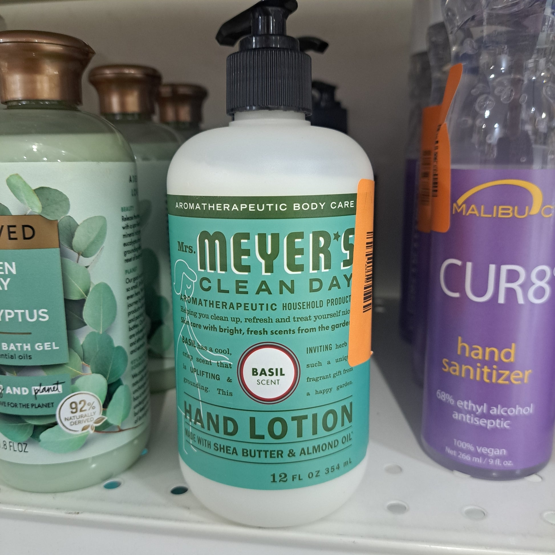 A bottle of Mrs. Meyers Hand Lotion with a basil scent sits on a store shelf, surrounded by other personal care products.