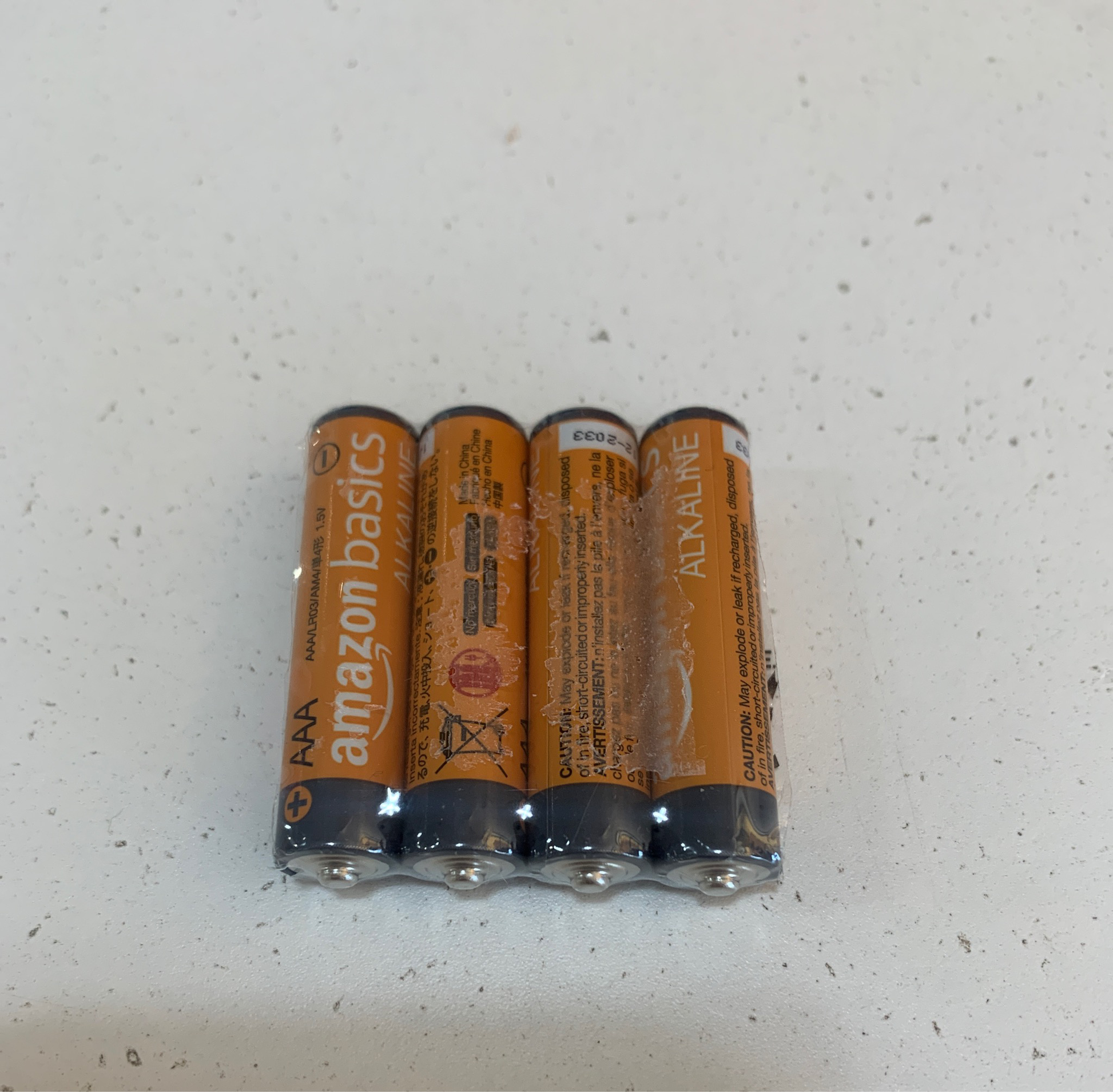 Four AAA batteries from Amazon Basics are neatly lined up on a spotless white surface, highlighting the handy 4-pack option.