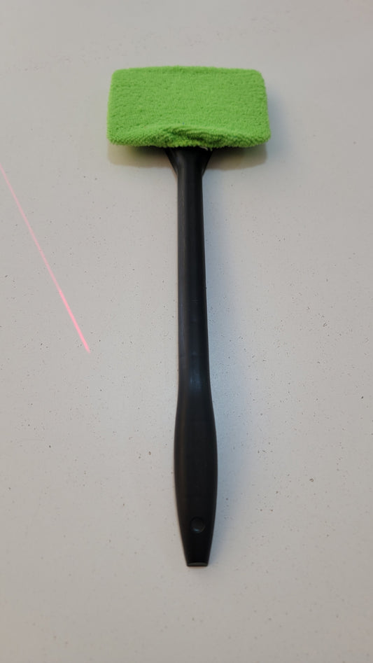 A Window Wildshield Cleaner with a long handle in green and black, placed on a light-colored surface.