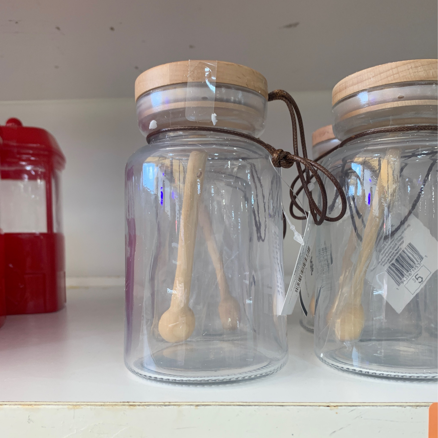 Jars with lids and one scoop inside are displayed on a shelf.