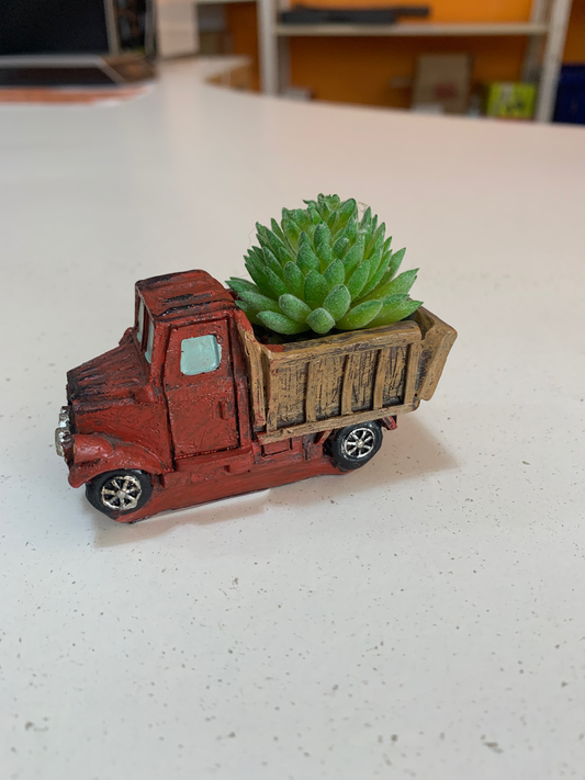 A Red & Green Plant Dump Truck features a faux plant on a white tabletop.