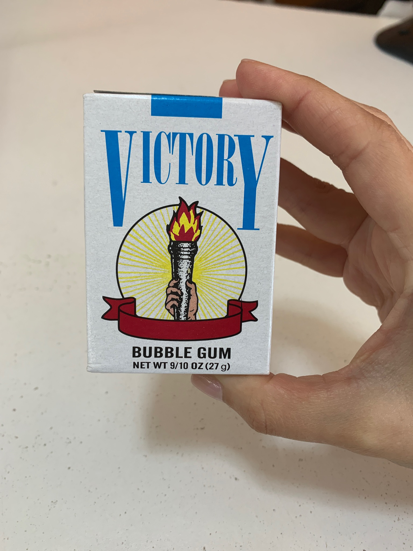 A hand holding a Bubble Gum Cigarettes box with a torch image on it. The box indicates a net weight of 27 grams.