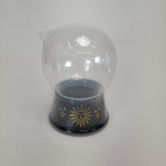 Introducing the Halloween "Crystal Ball" container: a clear glass globe adorned with a black base featuring intricate gold celestial designs. The top of this enchanting globe comes partially wrapped in protective plastic.