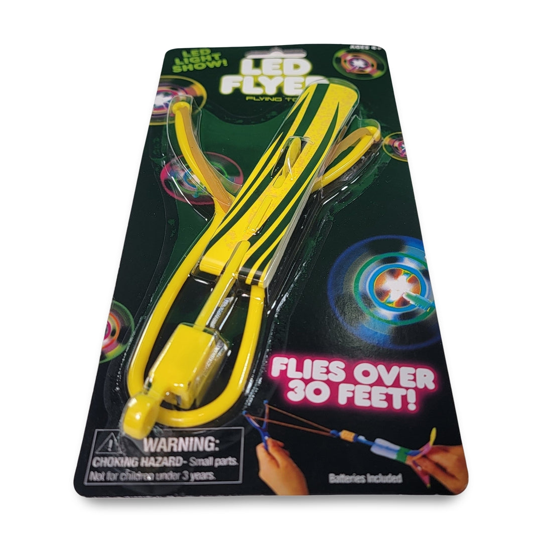 The LED flyer flying toy is a packaged slingshot-style toy that boasts the ability to fly over 30 feet. It comes with warnings regarding small parts and batteries.