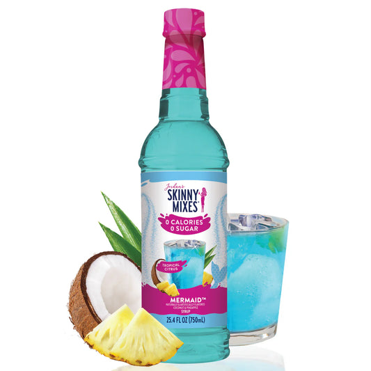 A bottle of Jordan's Skinny Syrup Mermaid, Sugar Free, 25.4oz with tropical citrus flavor, beside a glass of blue drink with ice, a coconut half, and pineapple slices.